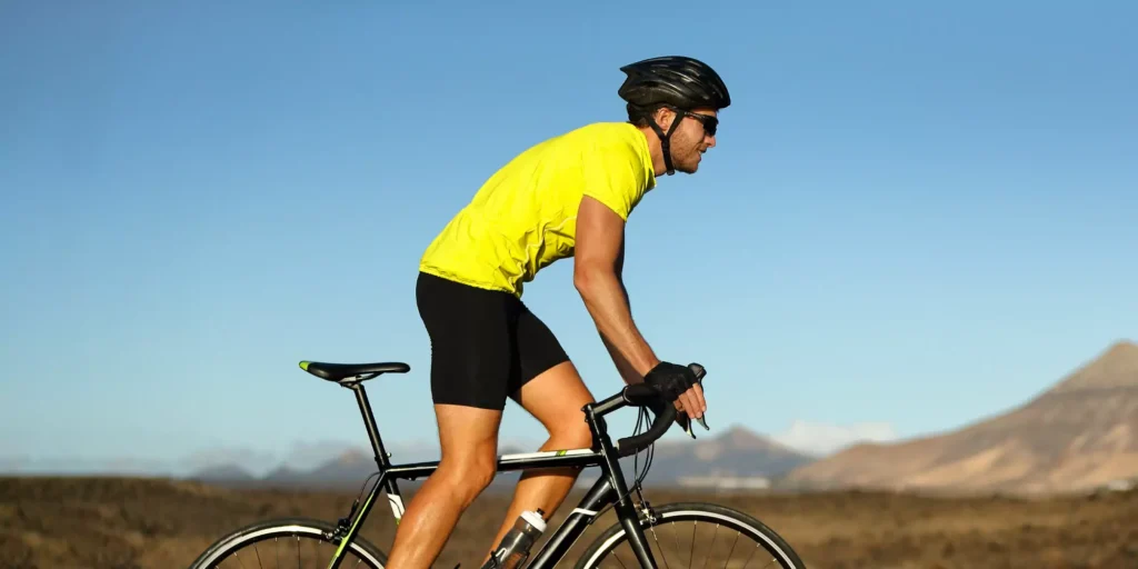 A cyclist in a bright yellow jersey rides a road bike through a vast, barren landscape, with clear blue skies and distant mountains, evoking adventure.