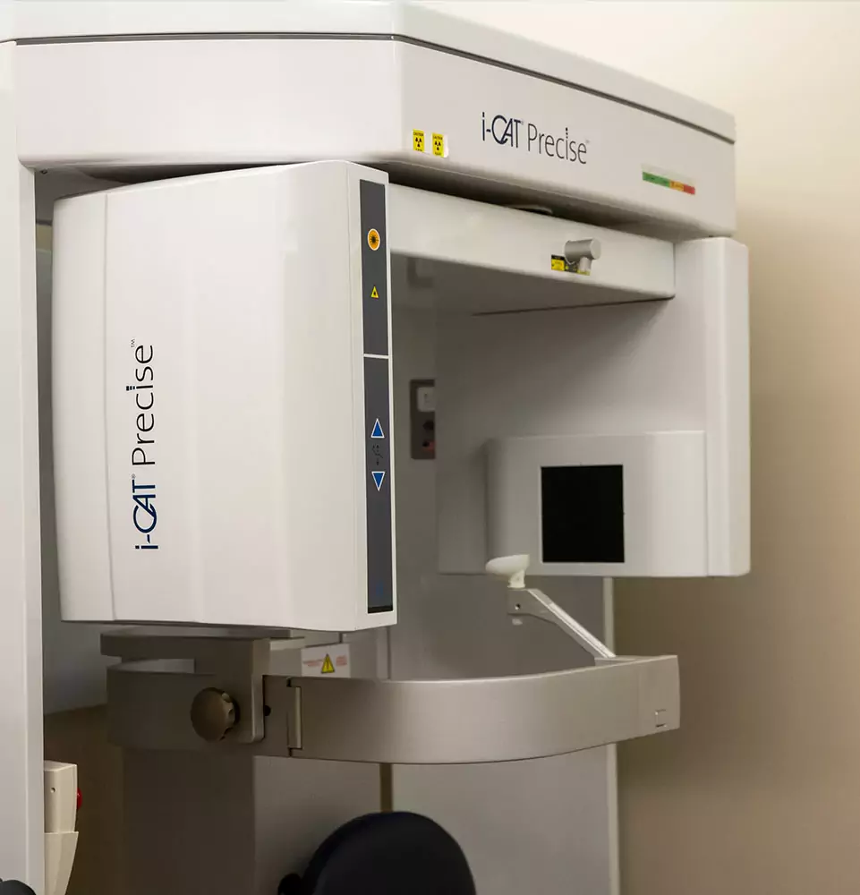 Dental CBCT machine in a clinic setting. The sleek white equipment features control buttons and a screen, indicating advanced imaging technology.