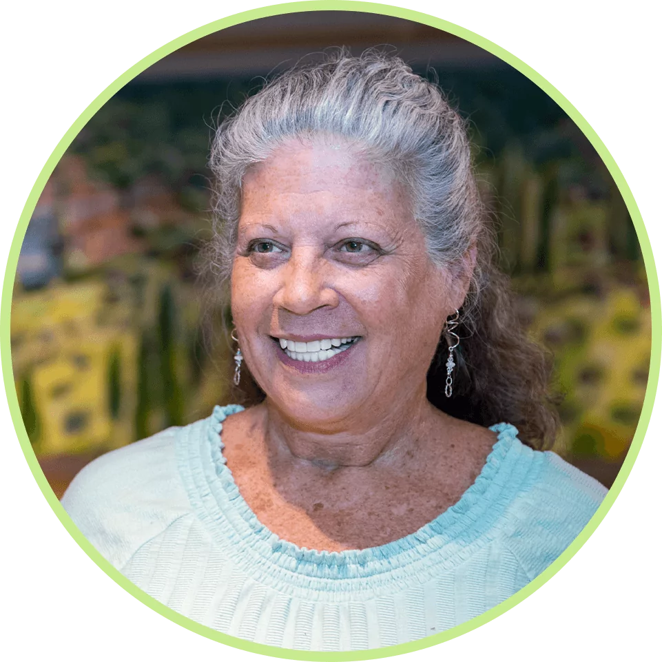 Smiling woman with gray hair and earrings, wearing a light blue top. Blurred colorful background, conveying a warm and cheerful mood.
